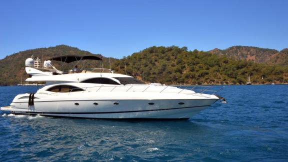 The motor yacht Act cruising on the sea, surrounded by green mountains and blue sky.